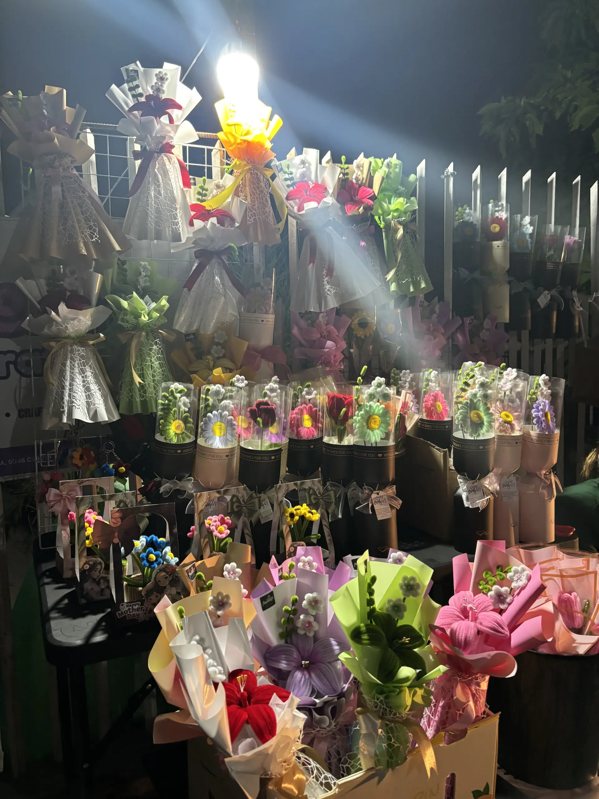 FleurKraft display at night — full range of bouquets, cylinders, and mini pots on show
